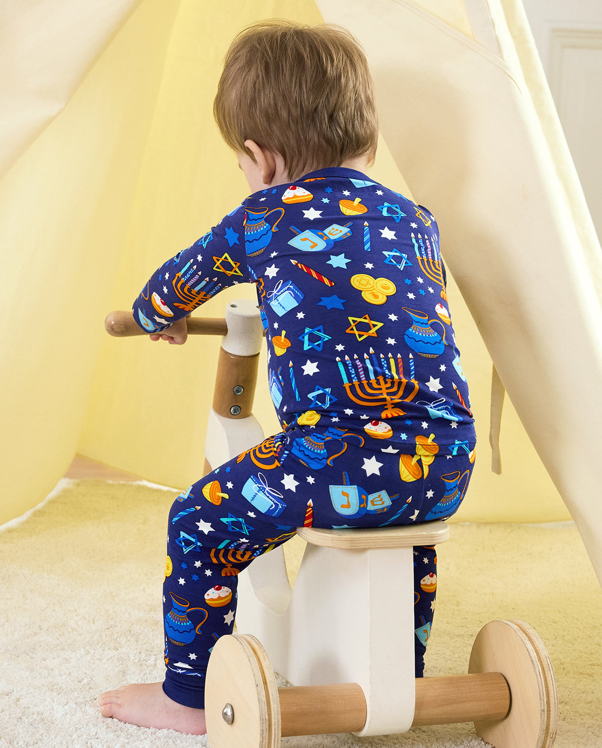 Rear view of a child seated on a wooden tricycle in the Hanukkah Magic two-piece set.