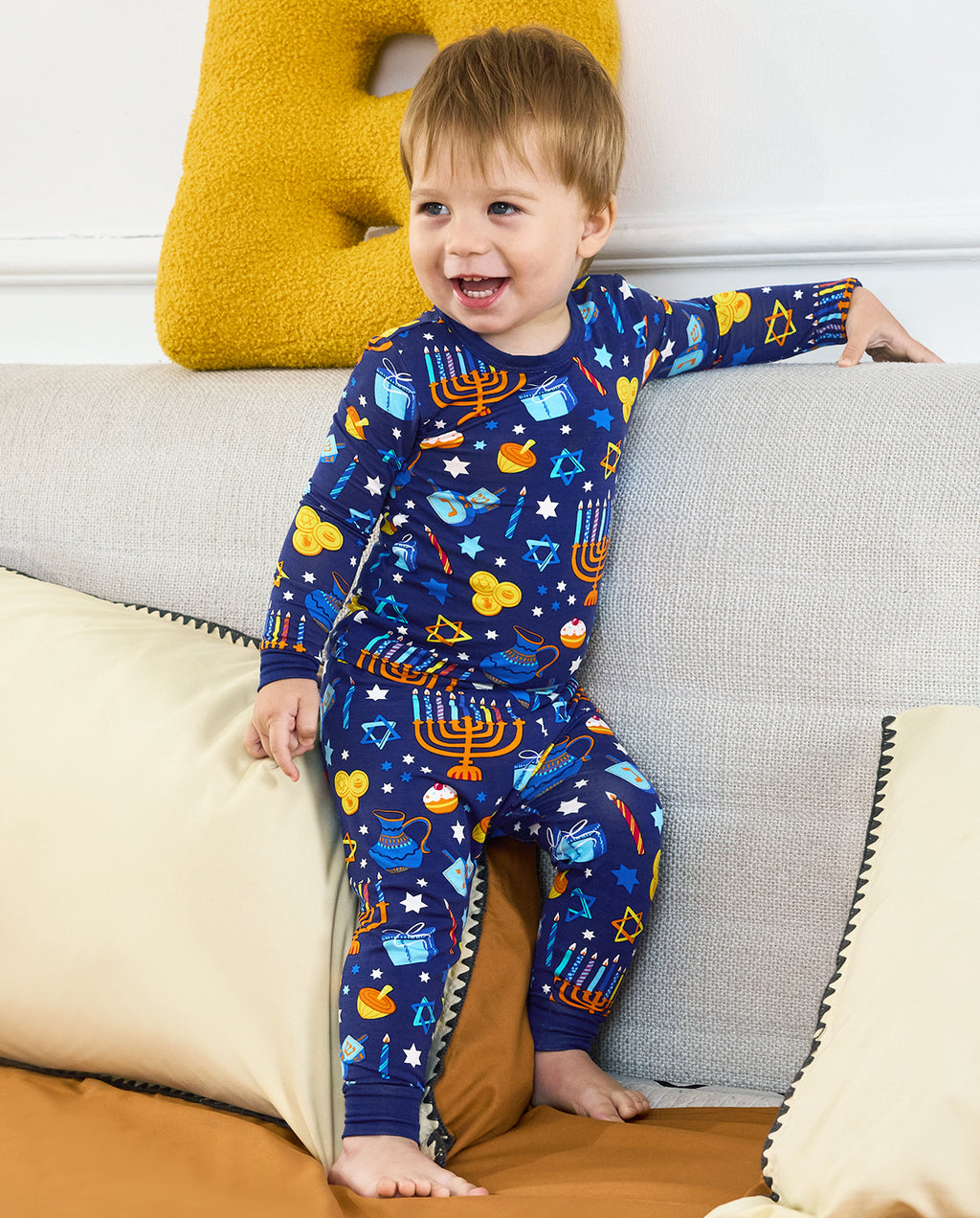 Child smiling while seated on a sofa in the Hanukkah Magic long-sleeve pajama set.