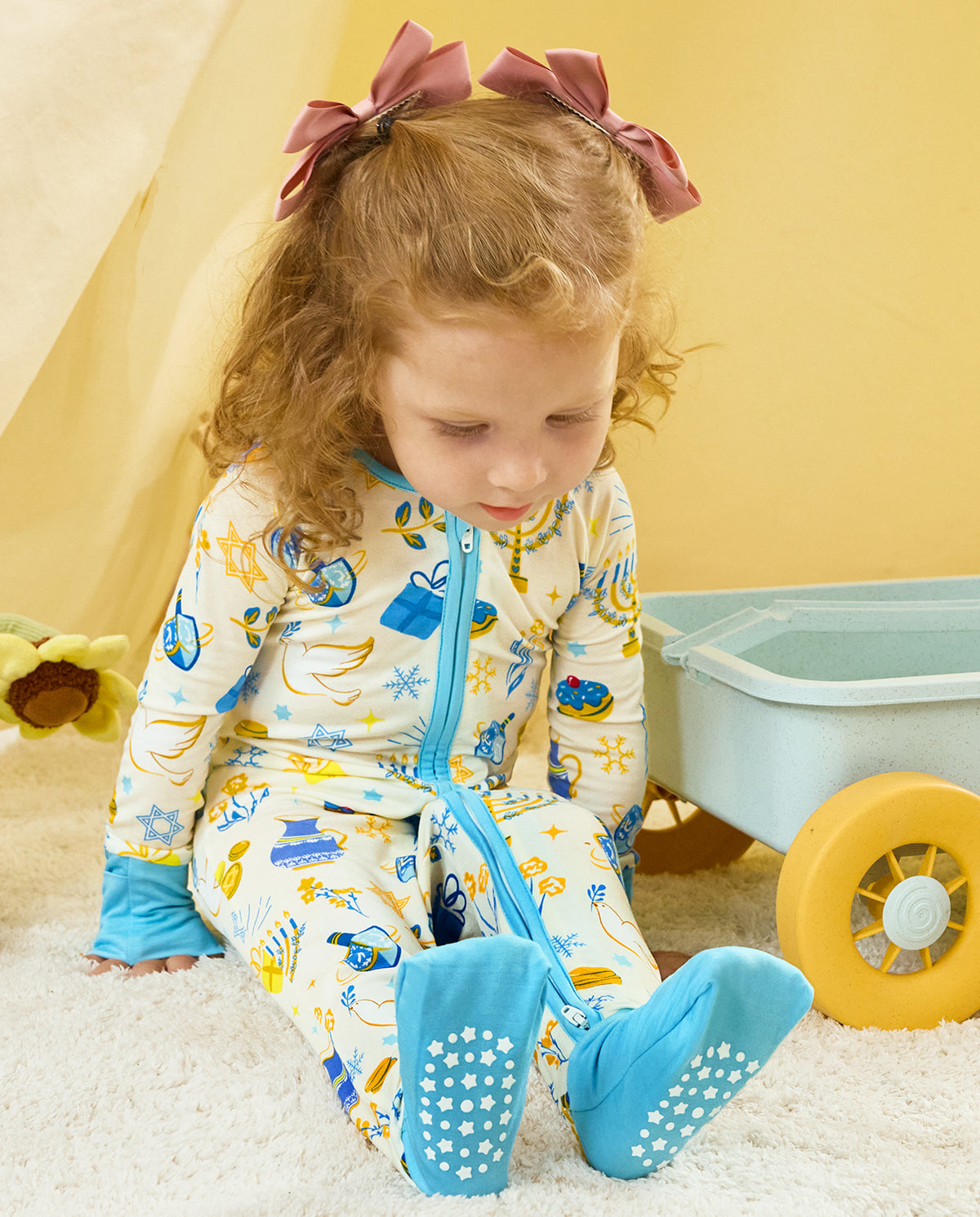 Child seated beside a small cart in the Happy Hanukkah zip-up romper.
