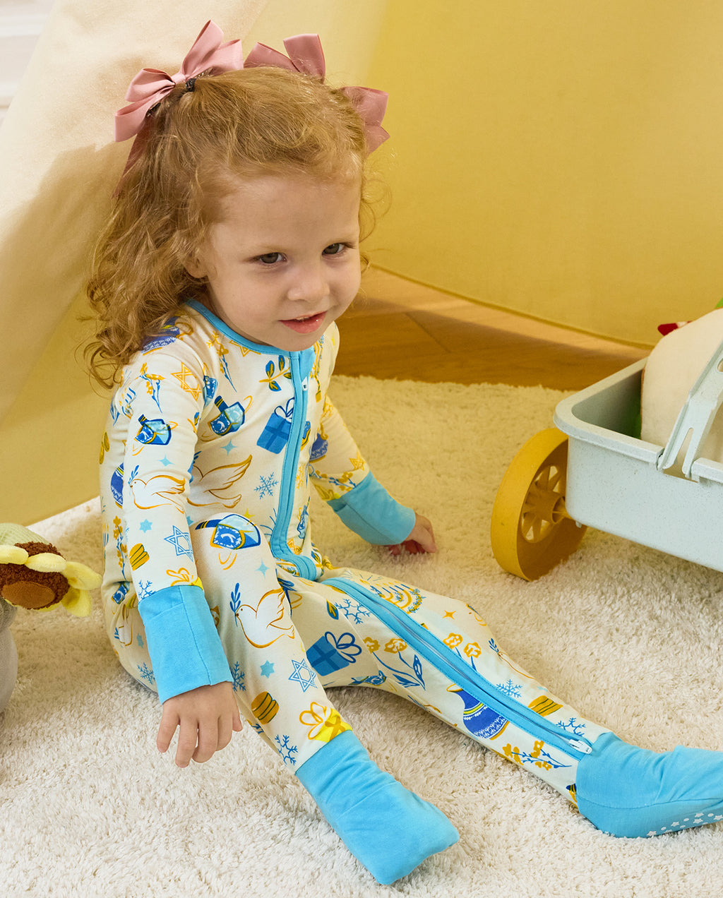 Child seated on a rug in the Happy Hanukkah romper, showing light blue foot cuffs and white sole grips.