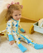 Child seated on a rug in the Happy Hanukkah romper, showing light blue foot cuffs and white sole grips.