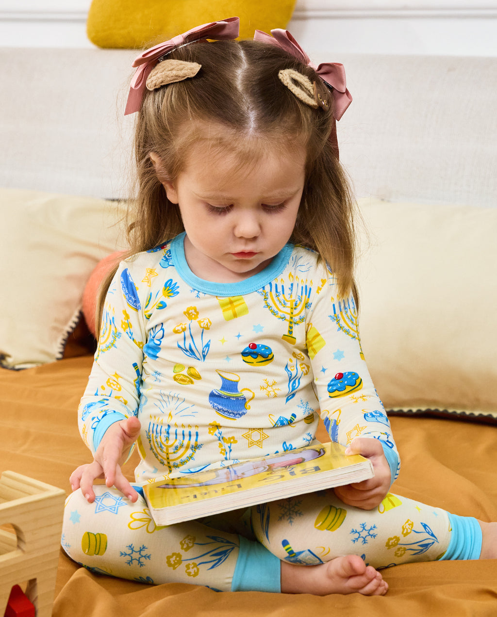 Child reading a book while seated on bedding in the Happy Hanukkah two-piece set.