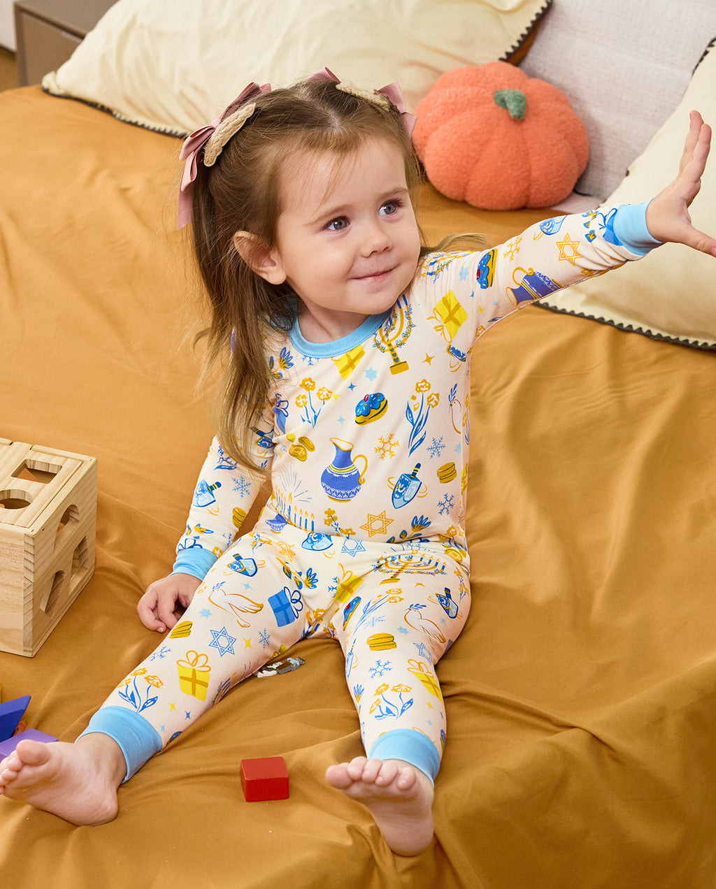 Child seated on bedding with one arm raised in the Happy Hanukkah pajama set.