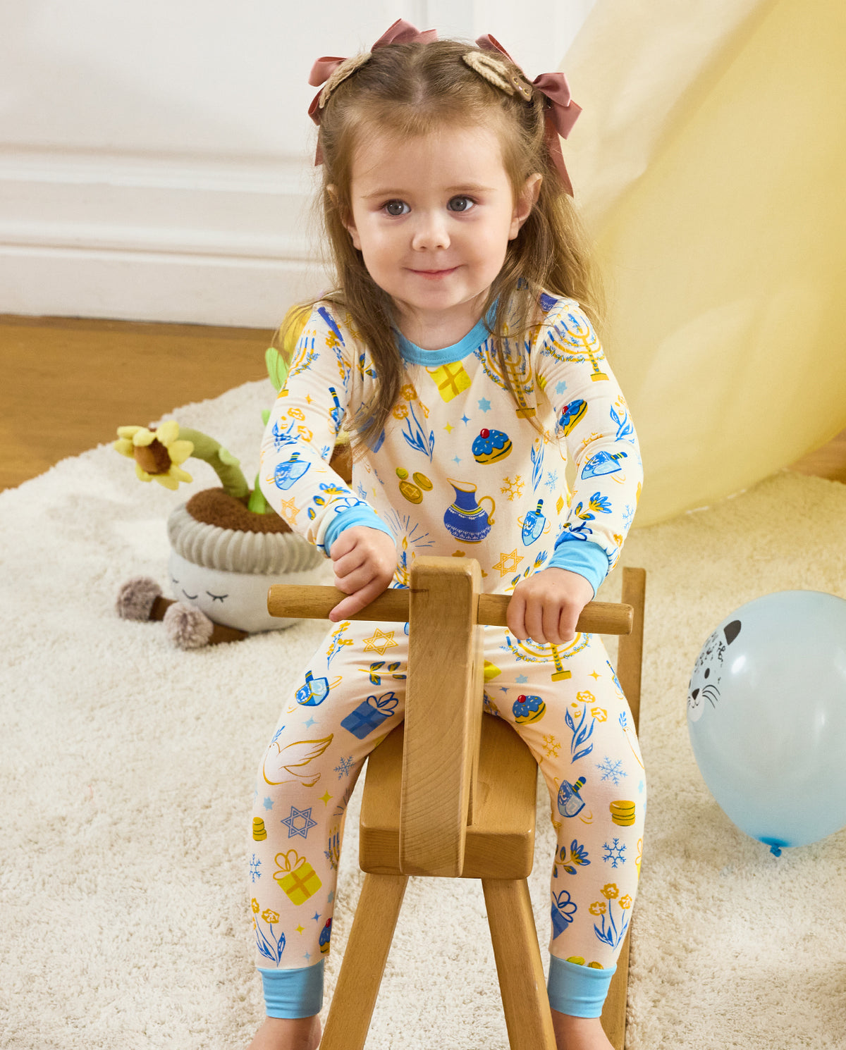 Front view of a child holding a wooden rocking horse in the Happy Hanukkah two-piece set.