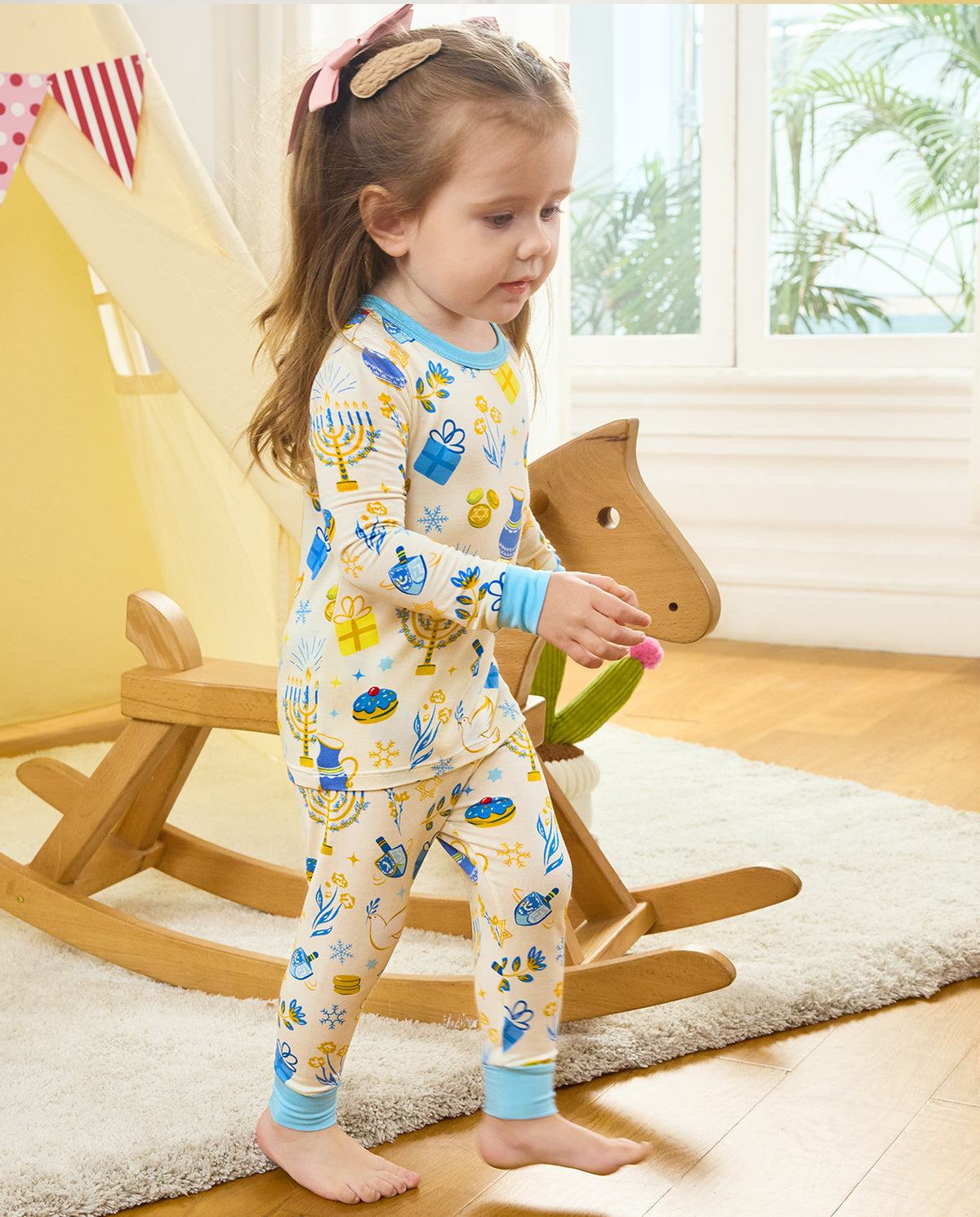 Child standing beside a wooden rocking horse, showing the Happy Hanukkah top and pants.