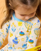 Close view of the Happy Hanukkah top with menorah, gift and treat motifs and light blue neckline.