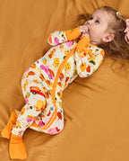 Child lying on orange bedding in a Harvest Farm zip-up romper with covered feet.