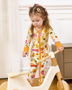 Front view of a child standing beside a wooden rocker in the Harvest Farm romper.