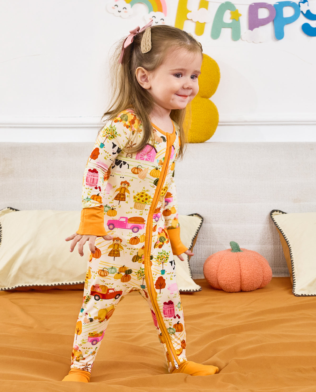 Smiling child standing on a sofa in the Harvest Farm zip-up romper.