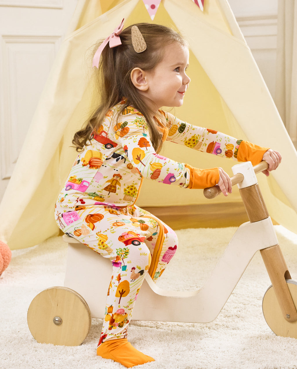 Side view of a child standing and holding a wooden rocker in the Harvest Farm romper.