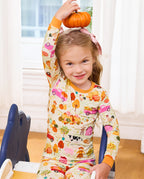 Child holding a pumpkin overhead in cream Harvest Farm pajamas with orange trim.