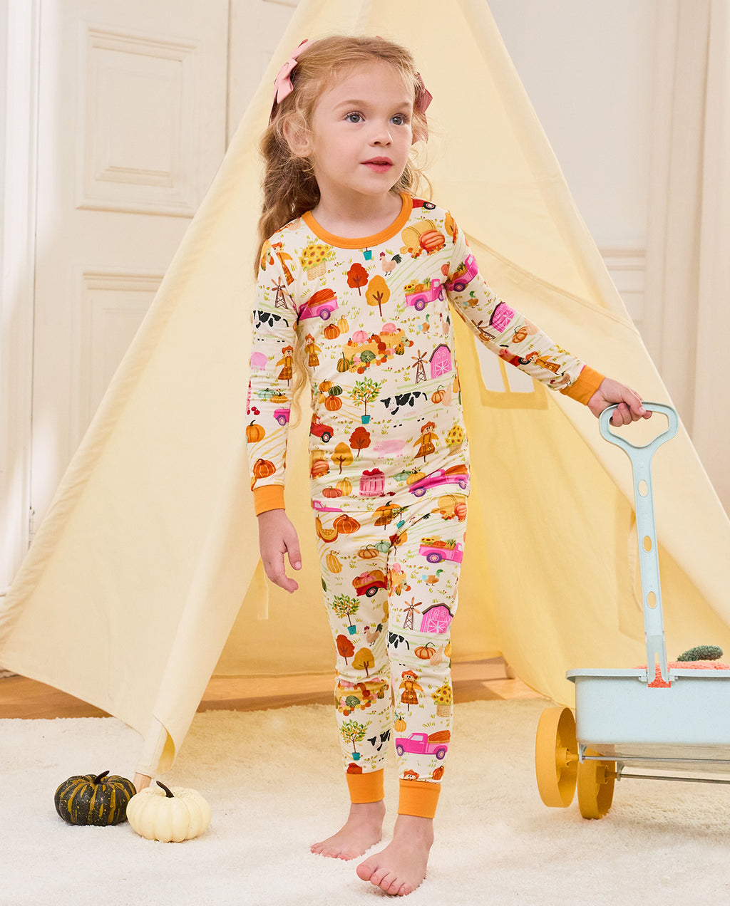Child standing beside a blue cart and play tent in the Harvest Farm pajama set.