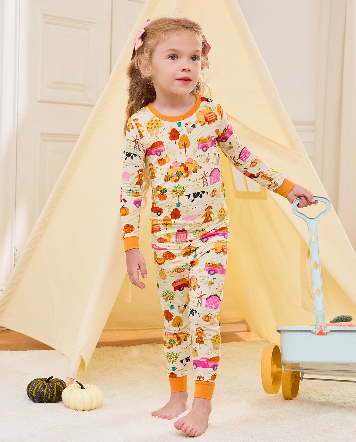 Child standing beside a blue cart and play tent in the Harvest Farm pajama set.