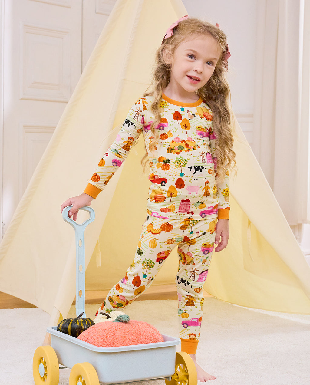 Smiling child holding a blue cart in Harvest Farm long-sleeve pajamas.