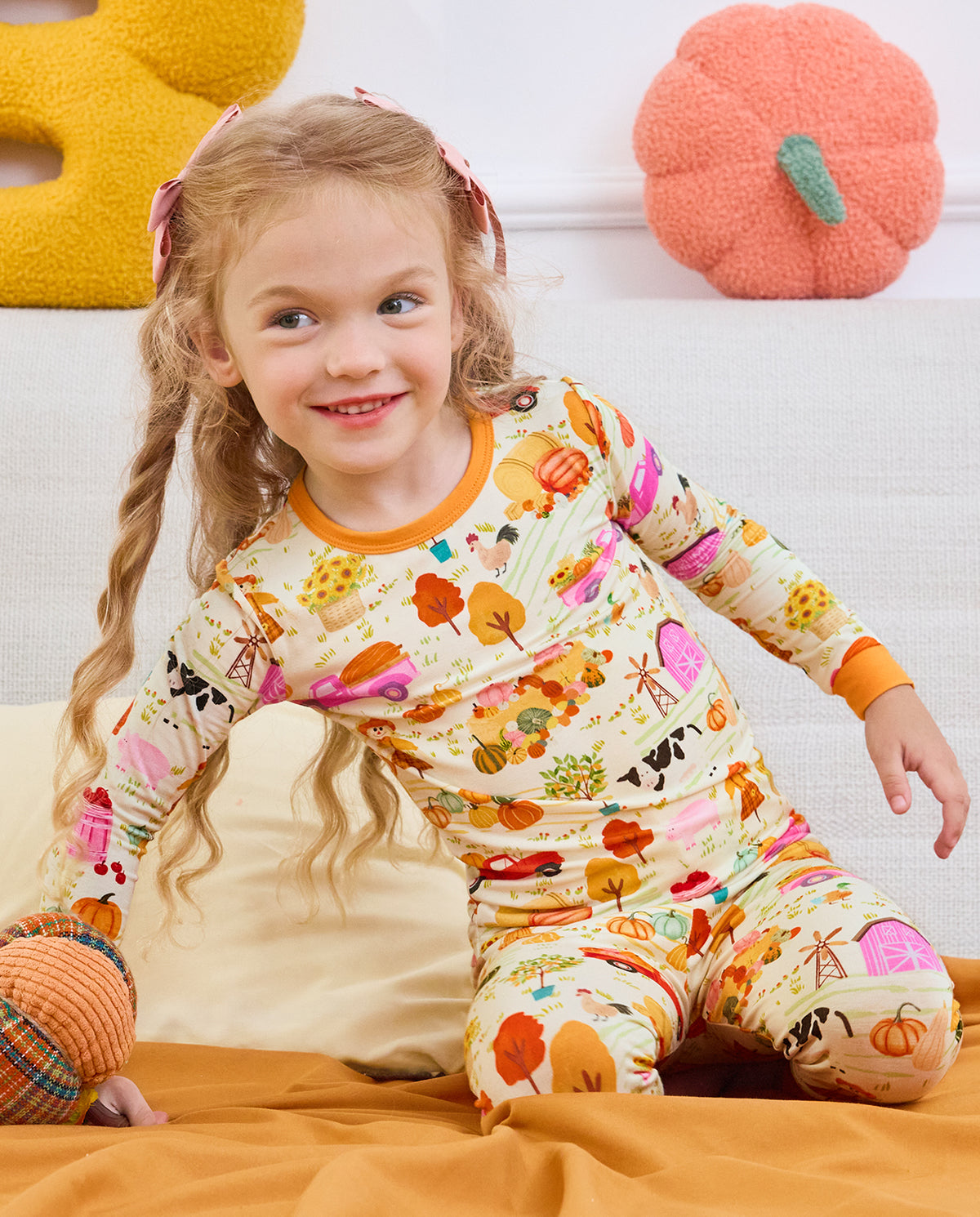 Side view of a child seated on a sofa wearing Harvest Farm pajamas.