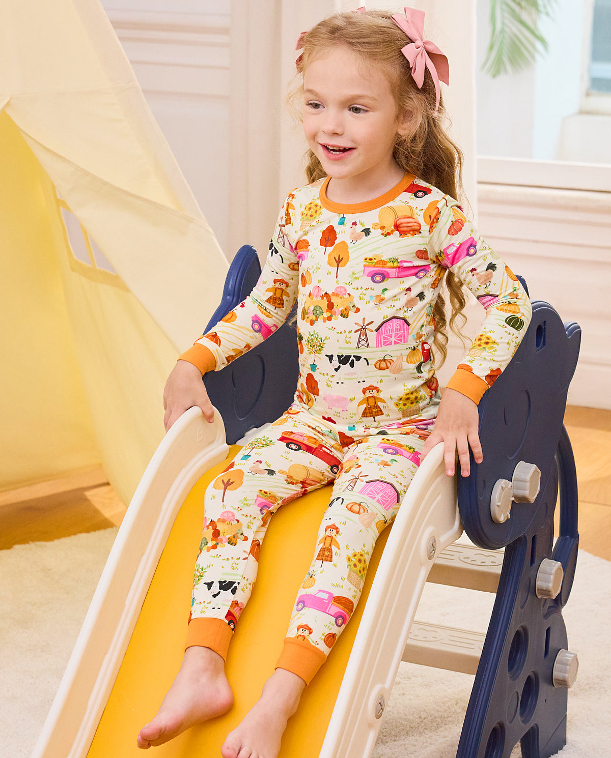 Child sitting on a blue slide in Harvest Farm pajamas with orange cuffs.