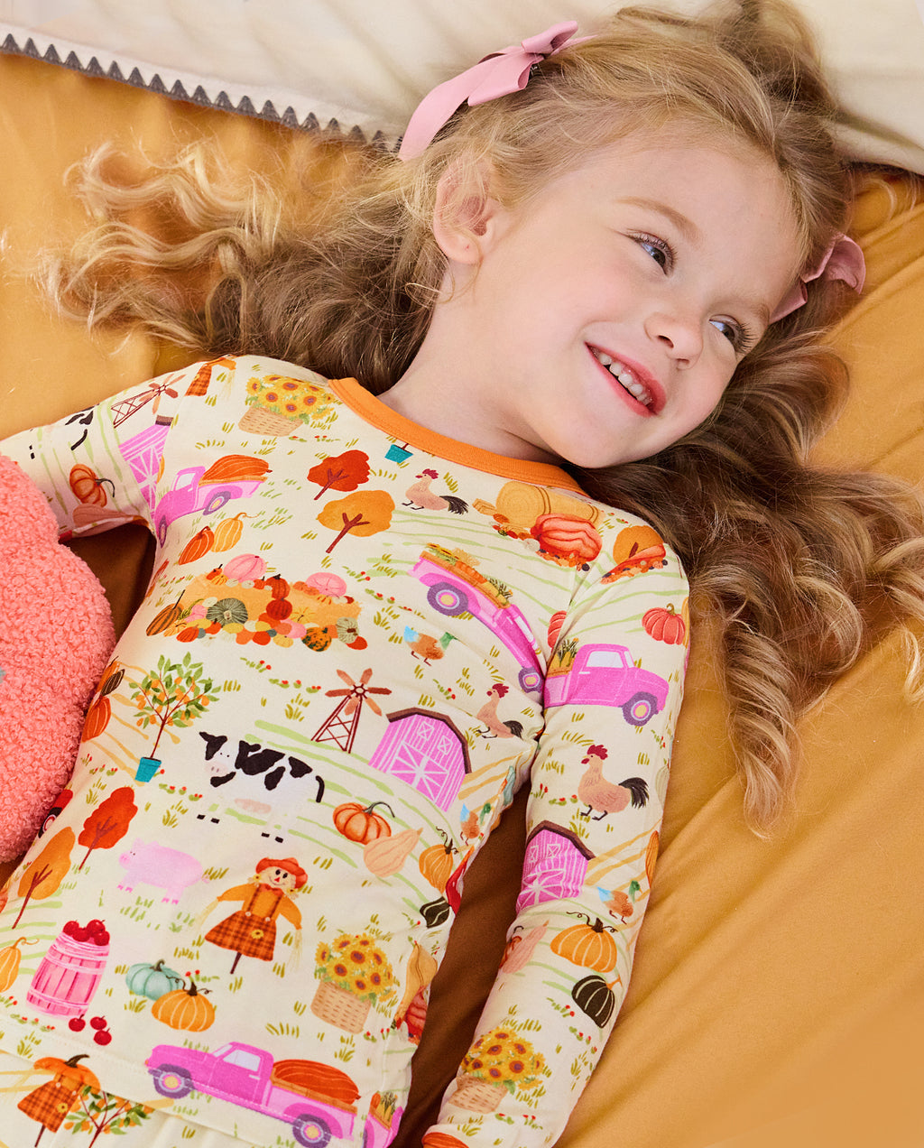 Child reclining on orange bedding in the Harvest Farm two-piece pajama set.