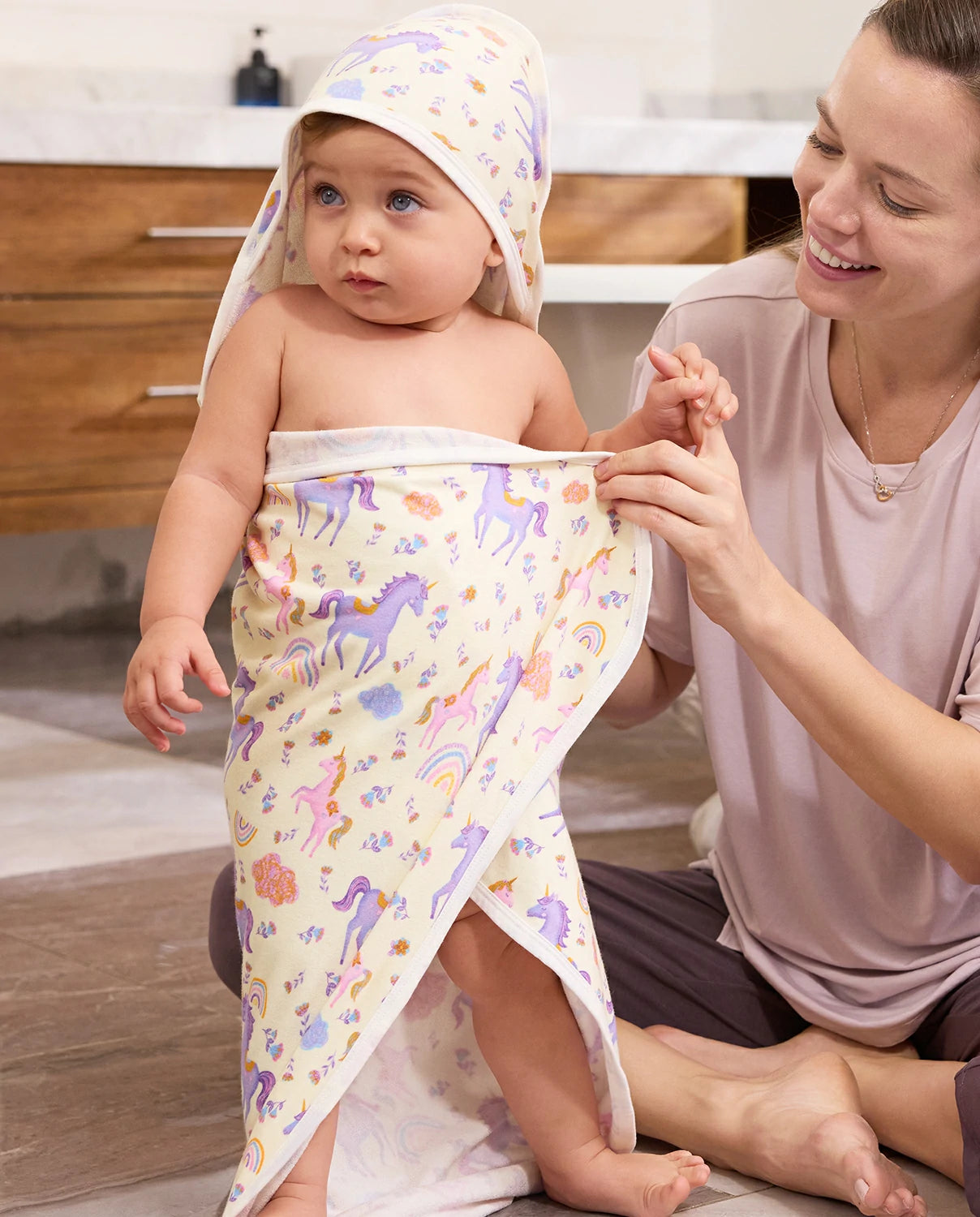 Lavender Unicorn Hooded Baby Bath Towels (2-Pack) - parent wrapping a baby in the unicorn-print hooded towel