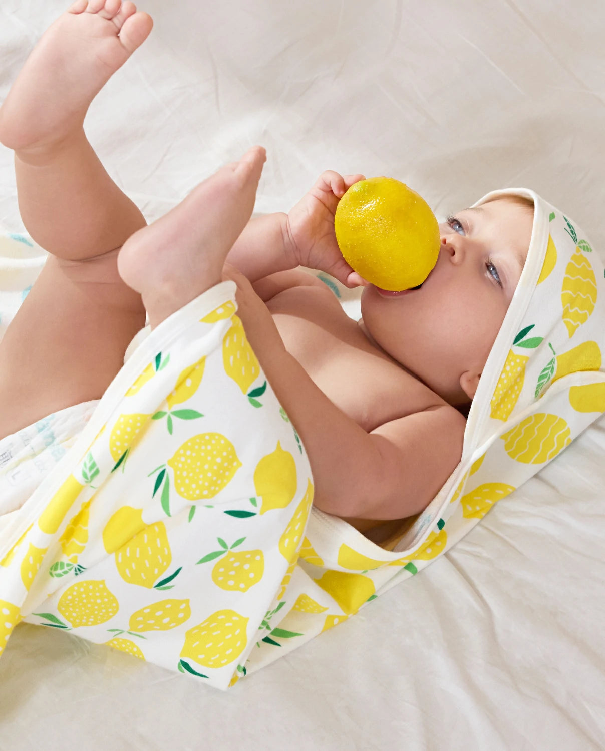 Lemon Tree Hooded Baby Bath Towels (2-Pack) - baby wrapped in the lemon-print towel while holding a lemon