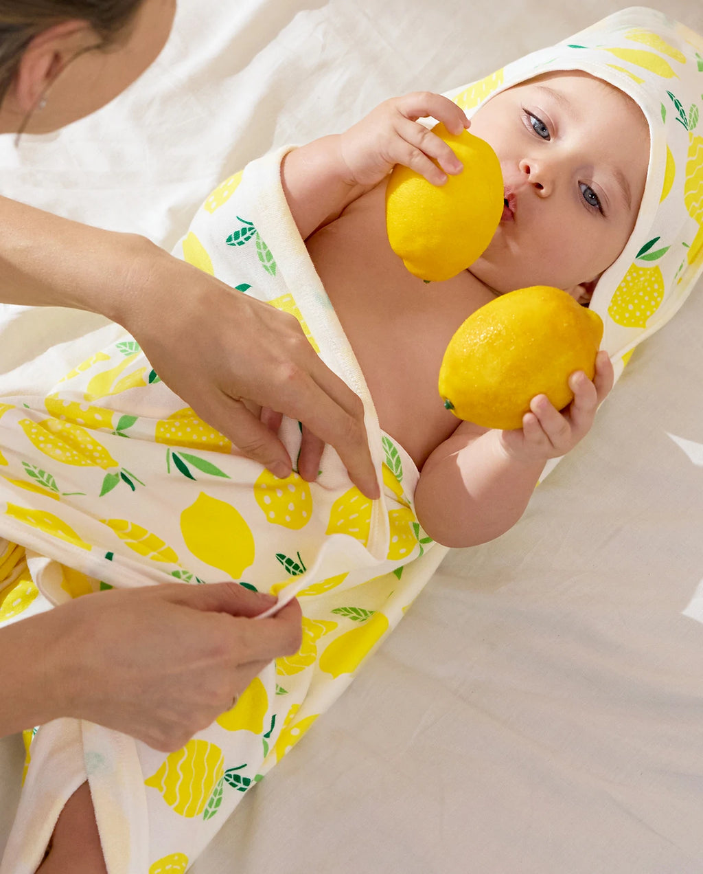 Lemon Tree Hooded Baby Bath Towels (2-Pack) - baby wrapped in the lemon-print towel while an adult holds two lemons
