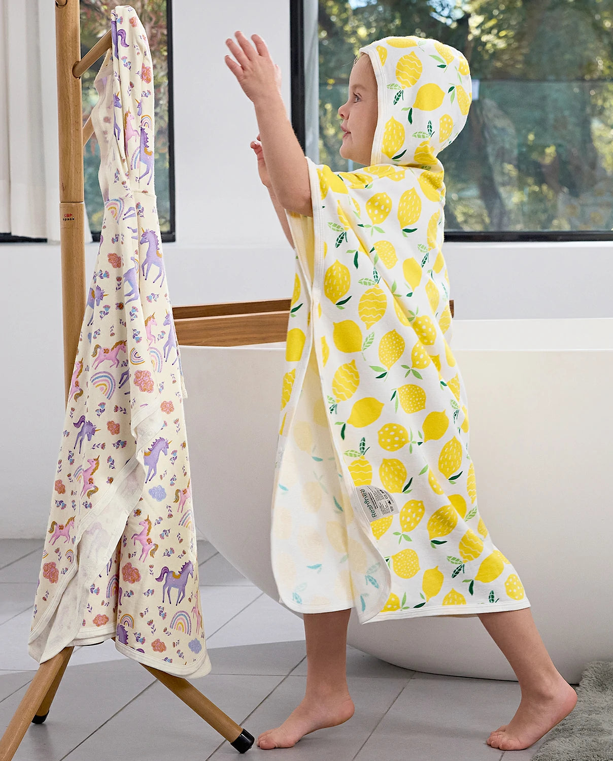 Lemon Tree Hooded Toddler Bath Towel - child wearing the hooded towel beside a towel rack, side view