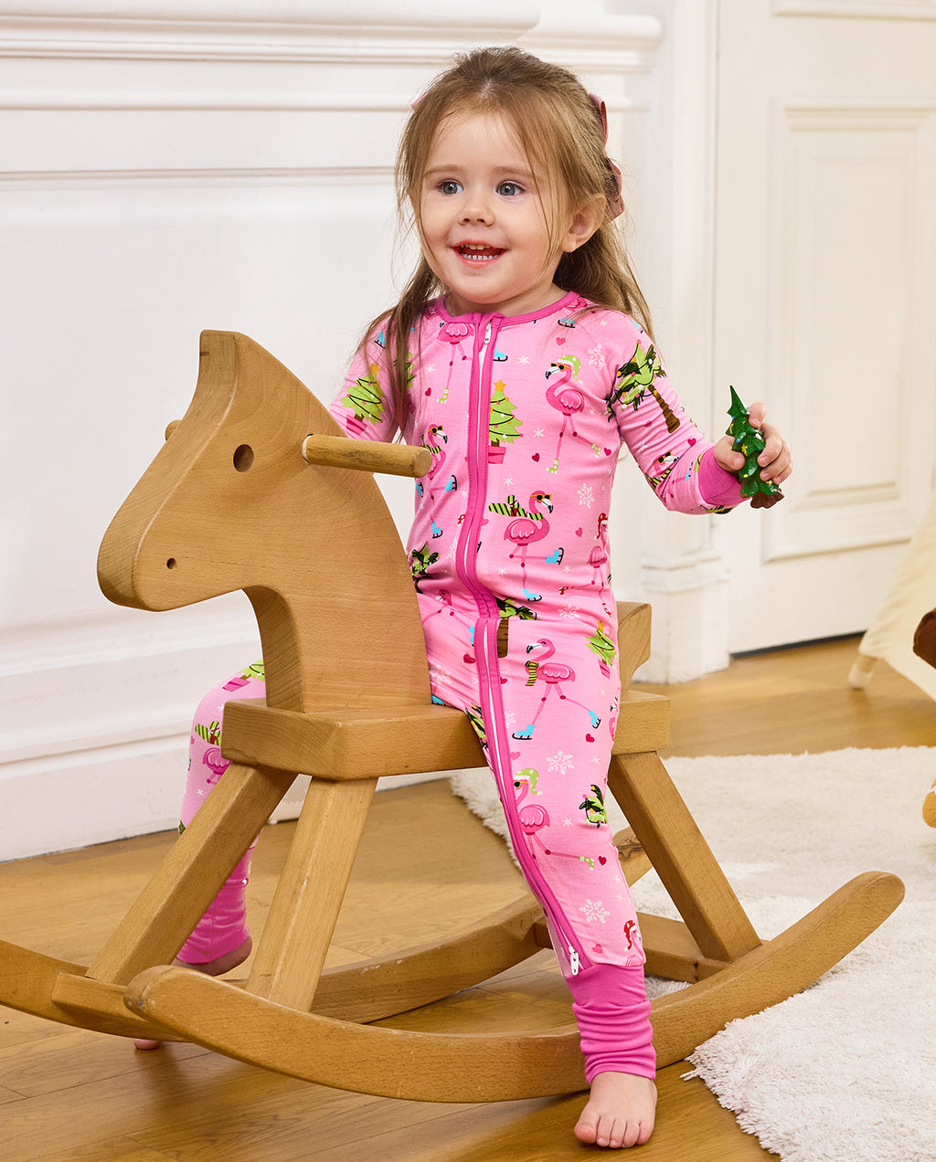 Child standing beside a wooden rocking horse with a toy in the Merry Mingo romper.