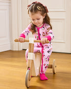 Child seated on a wooden tricycle in the pink Merry Penguins zip-up romper.