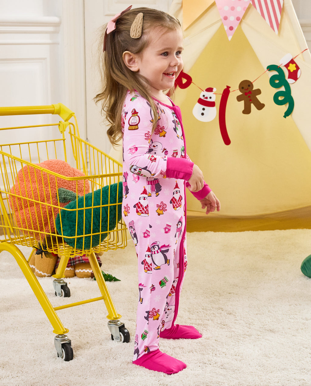 Side view of a child standing beside a yellow cart in the Merry Penguins romper.
