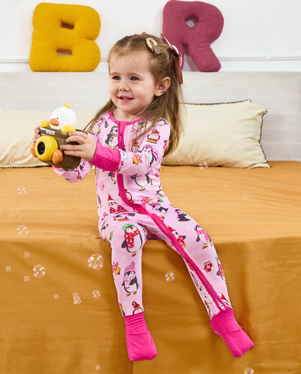 Child seated with a toy camera and bubbles in the Merry Penguins romper.