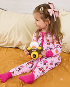 Child seated on bedding with a toy camera in the Merry Penguins romper.