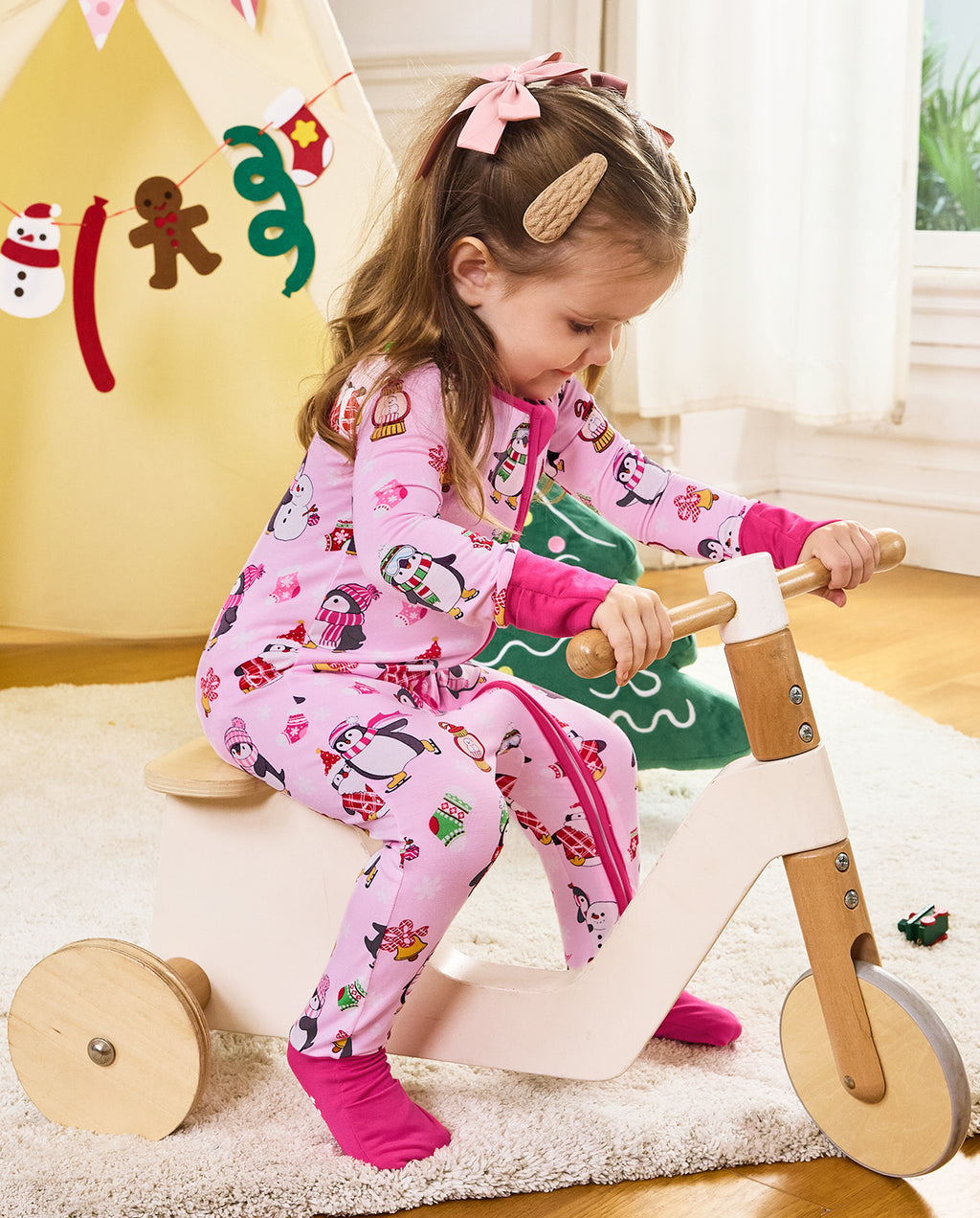 Child looking downward while riding a wooden tricycle in the Merry Penguins romper.