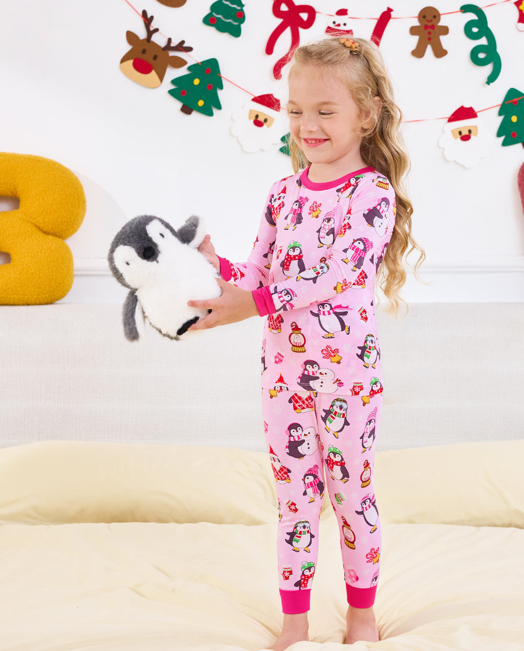 Child standing on a sofa holding a penguin plush in Merry Penguins pajamas.