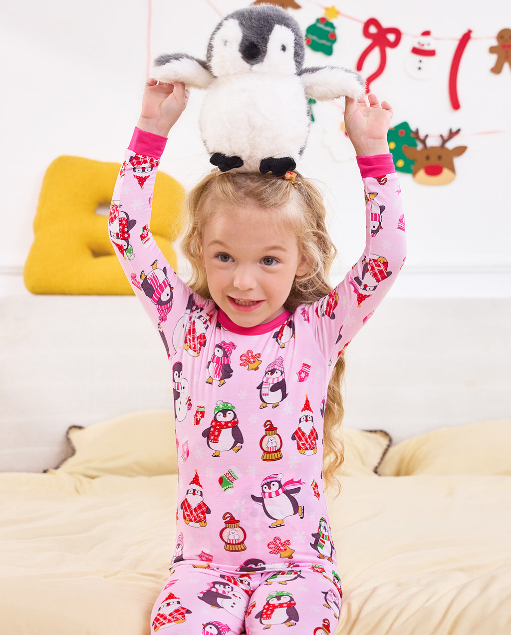 Close front view of a child holding a penguin plush overhead in Merry Penguins pajamas.