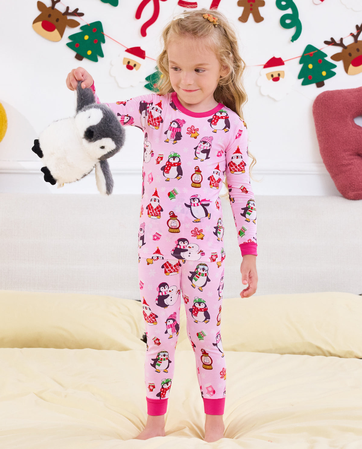Child holding a penguin plush to the side in the Merry Penguins pajama set.