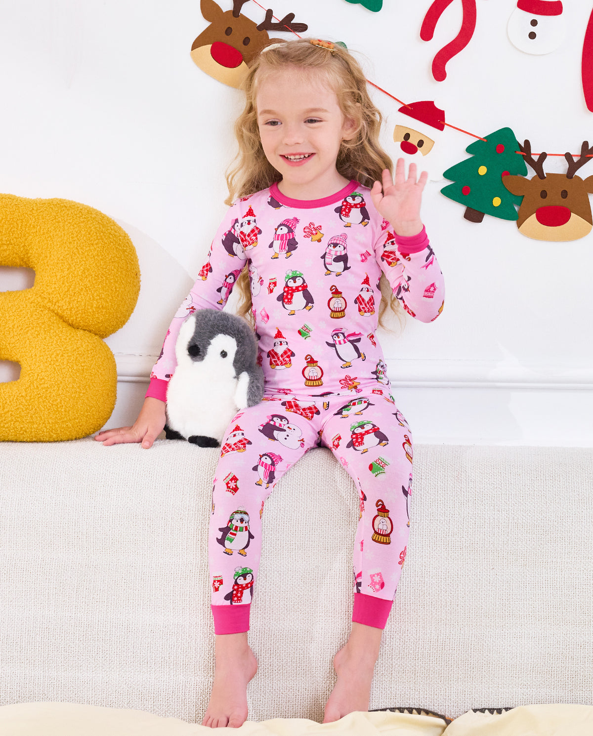 Child seated on a sofa with a penguin plush in Merry Penguins pajamas.