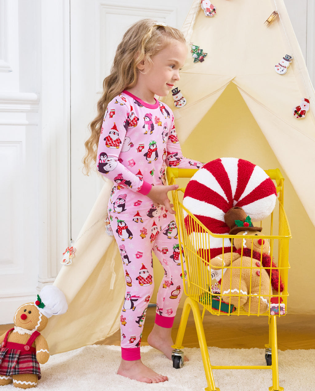 Side view of a child standing beside a yellow cart in Merry Penguins pajamas.