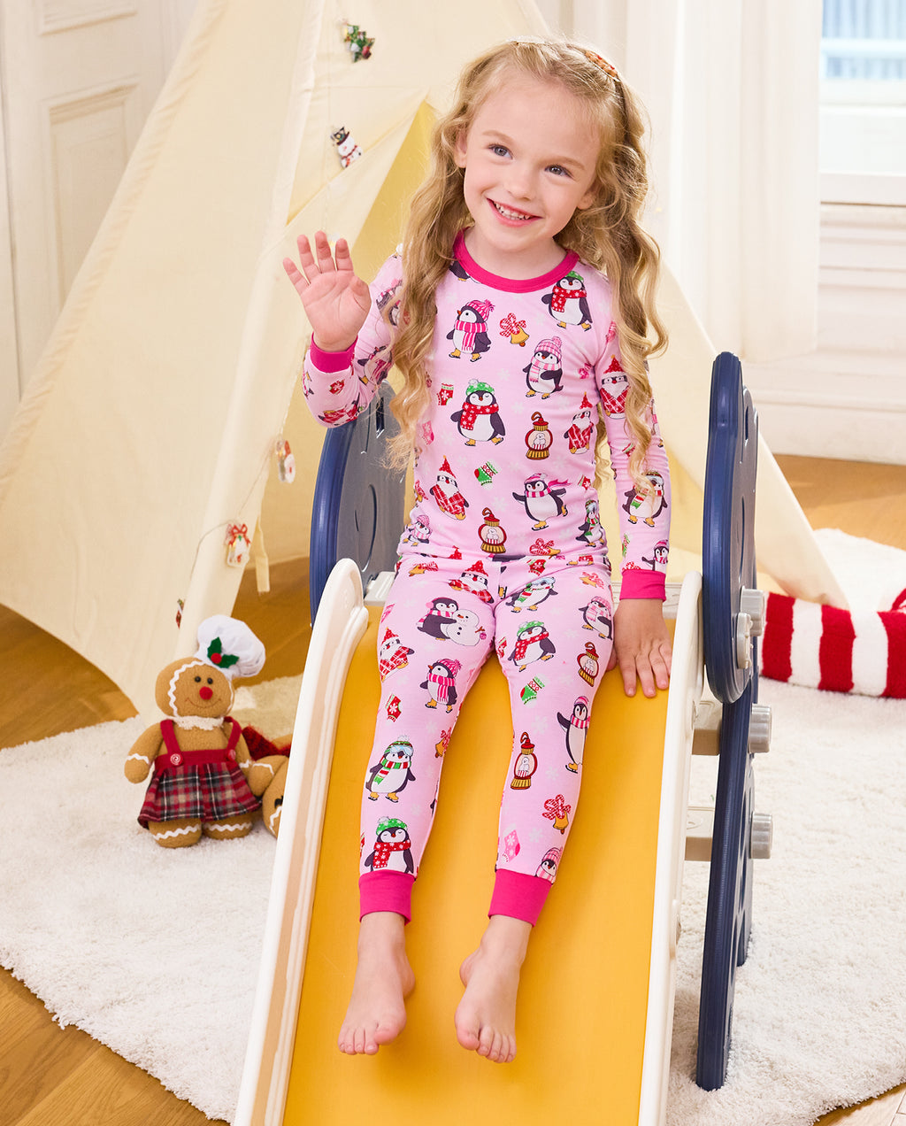 Child waving while seated on a slide in Merry Penguins pajamas.