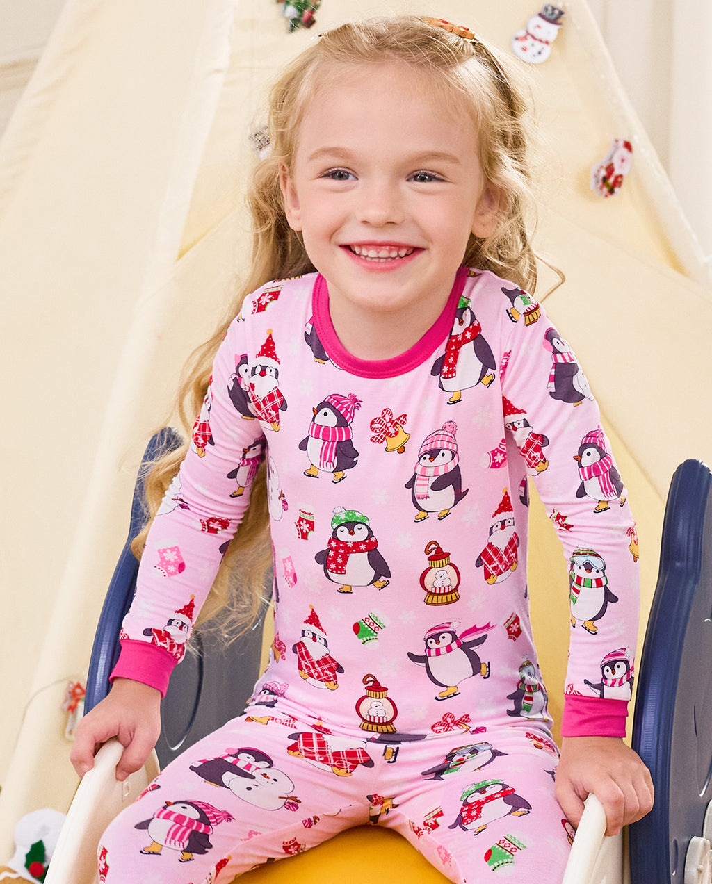 Close-up of a smiling child seated on a slide in the Merry Penguins long-sleeve top.