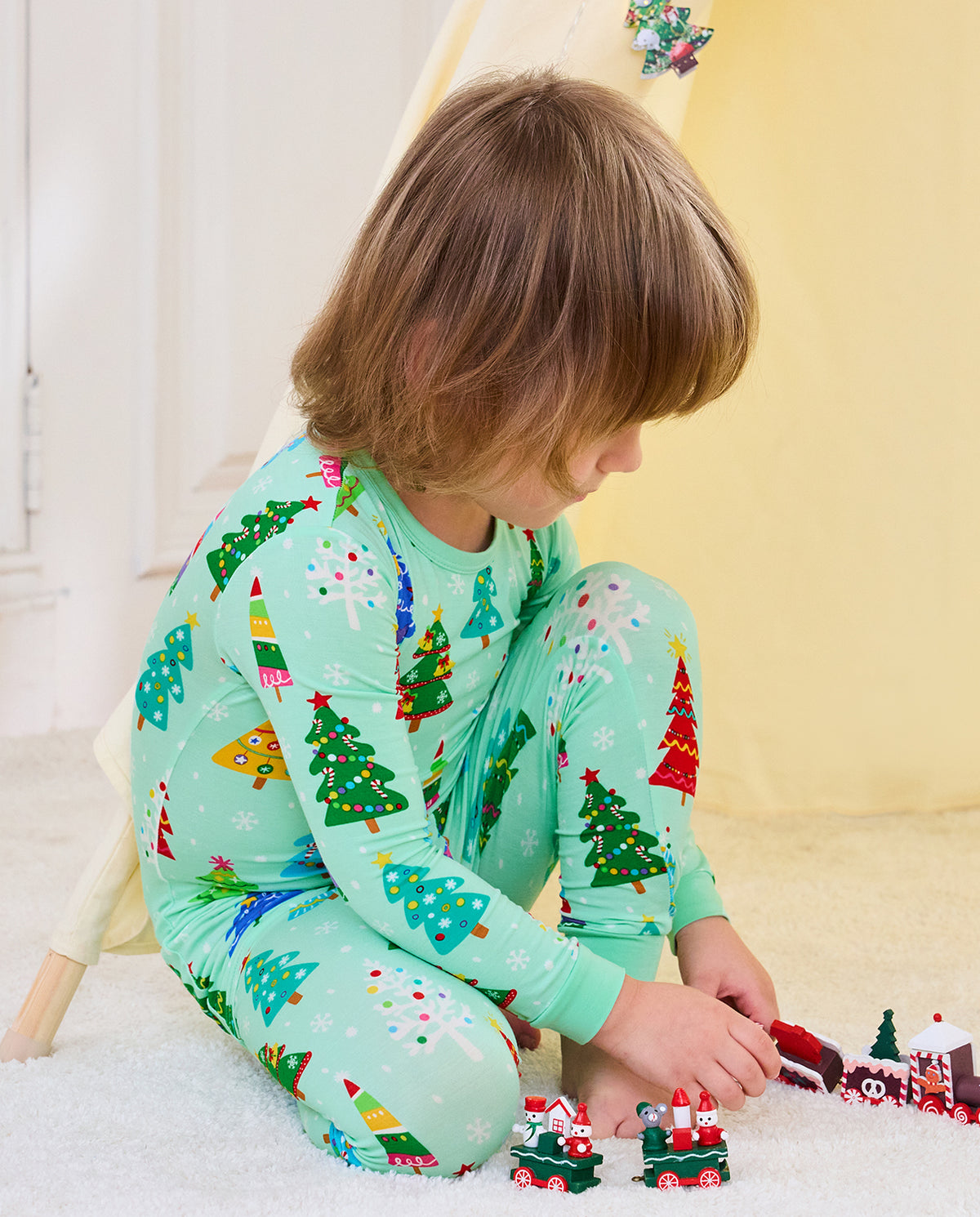 Side view of a seated child in Merry Trees mint-green pajamas playing with toy trains