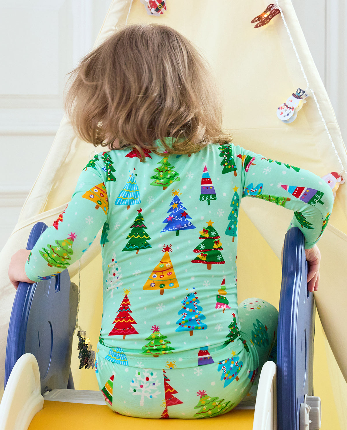 Child seated on a slide showing the back of Merry Trees Christmas-tree pajamas