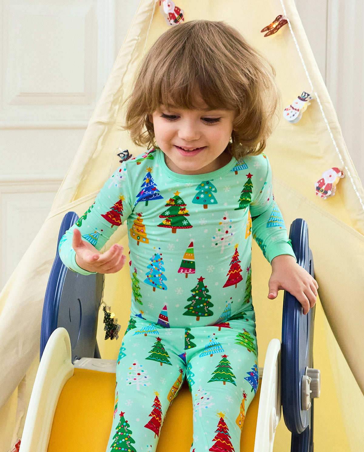 Front view of a smiling child in Merry Trees long-sleeve pajamas at a slide