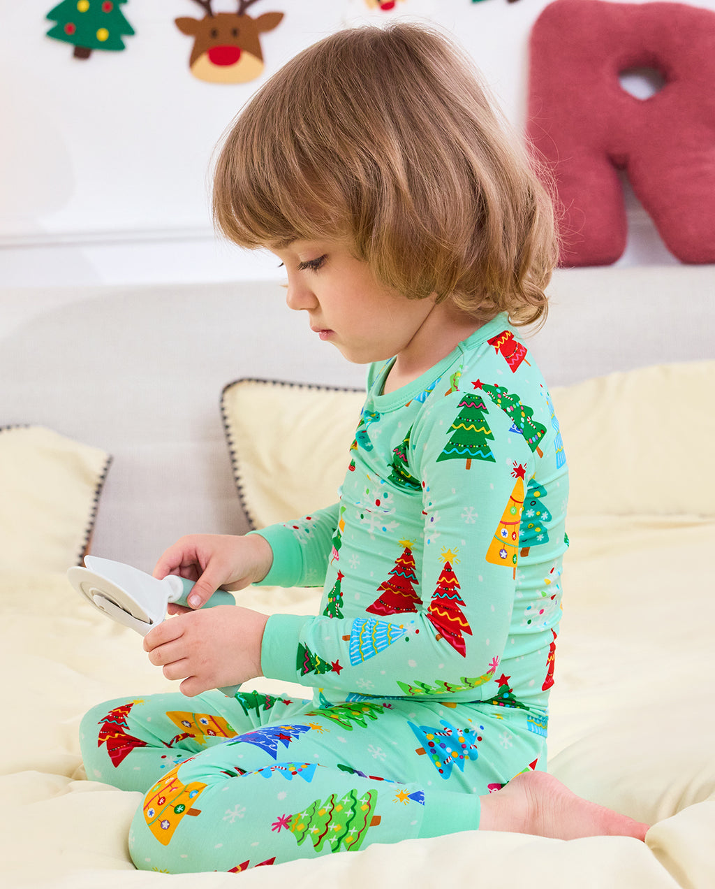 Child sitting on a sofa in Merry Trees pajamas while holding an open book