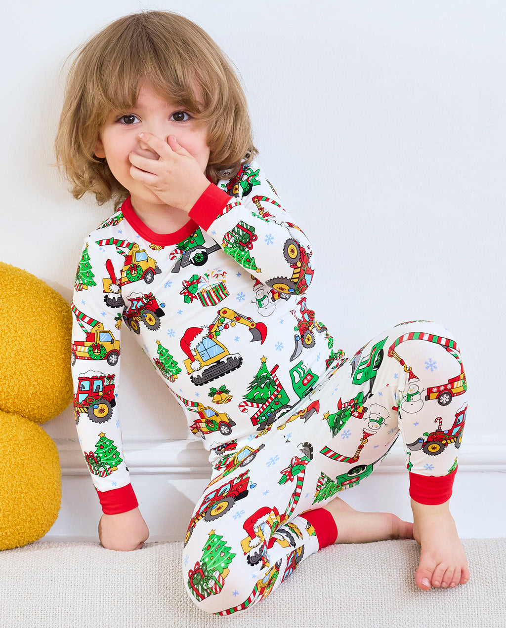 Child seated with one hand near the face in Merry Truckmas Christmas vehicle pajamas