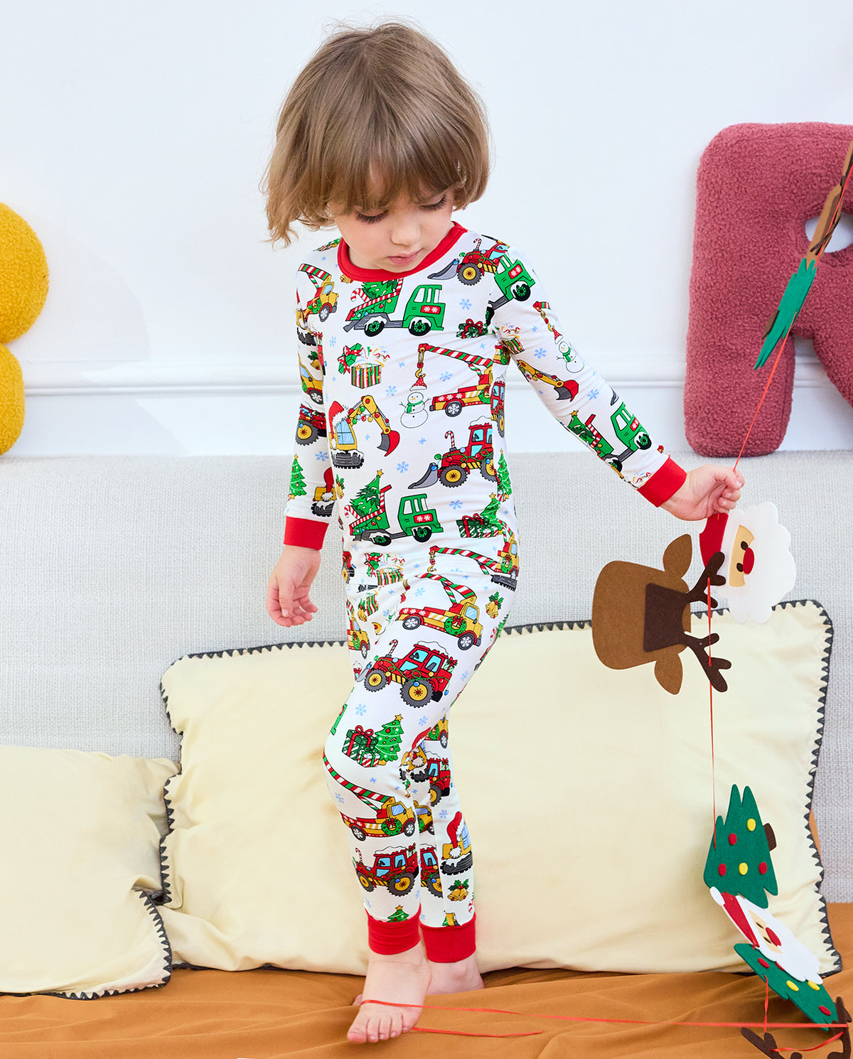 Full front view of a child standing on a sofa in Merry Truckmas pajamas