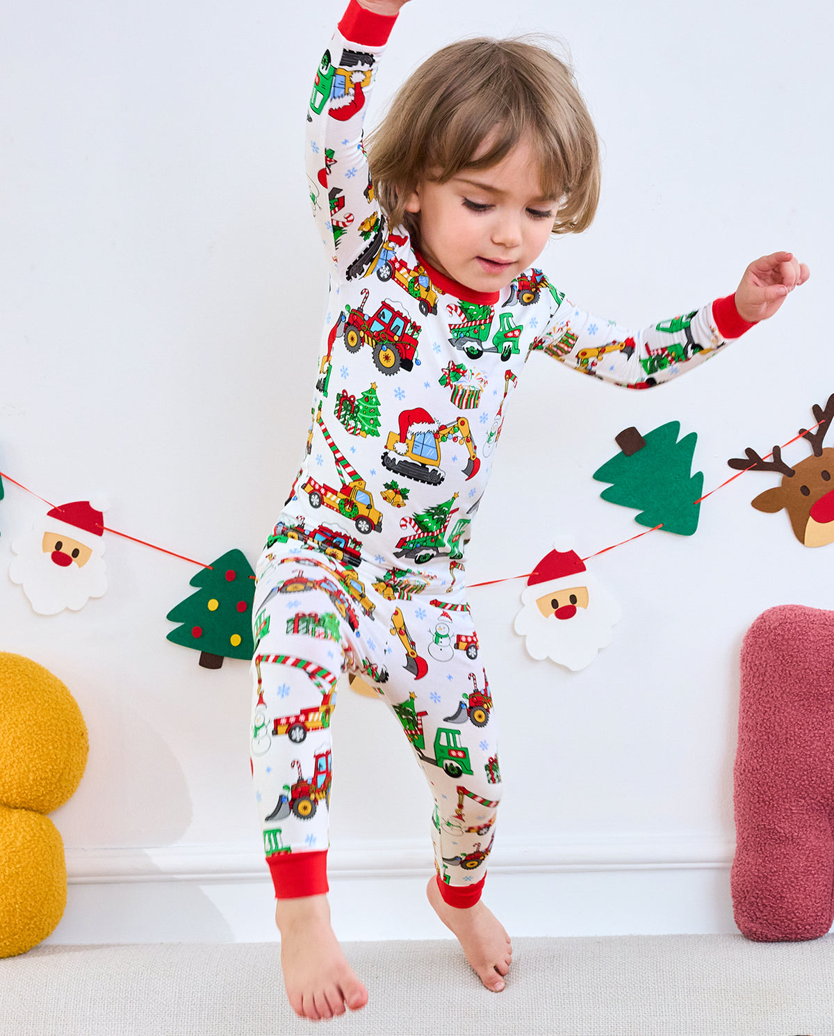 Child reaching upward in Merry Truckmas matching top and pants with red cuffs