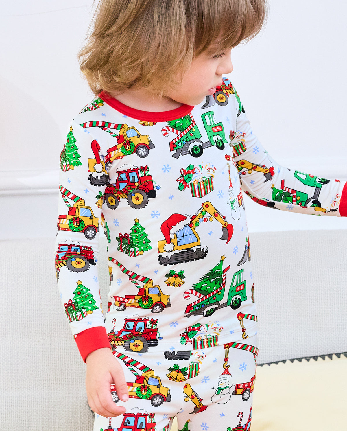 Child looking down at Merry Truckmas pajama top with decorated trucks and gifts