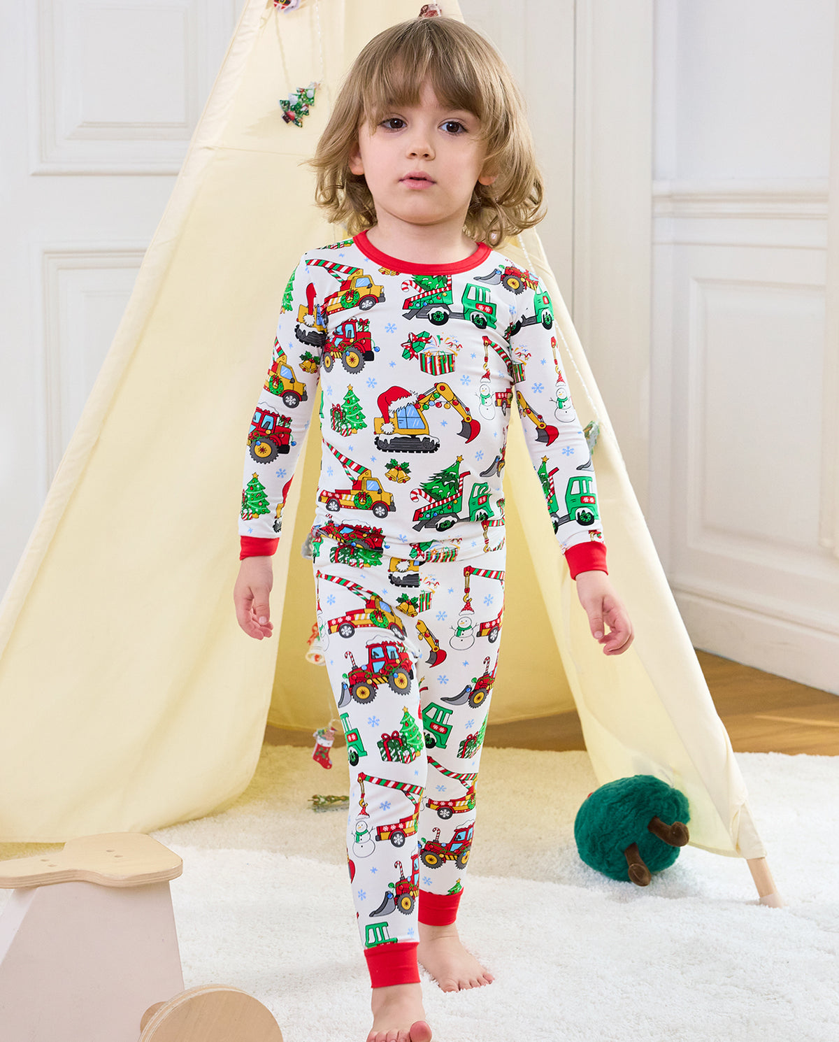 Child seated in front of a holiday tent wearing Merry Truckmas long-sleeve pajamas
