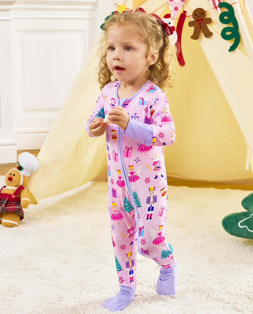 Child standing by a play tent holding a small object in the Nutcracker Fairy romper.