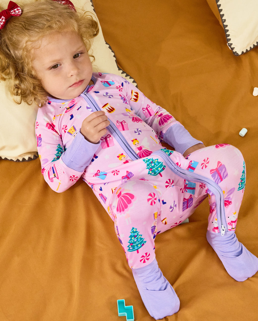 Child reclining on orange bedding in the Nutcracker Fairy zip-up romper.