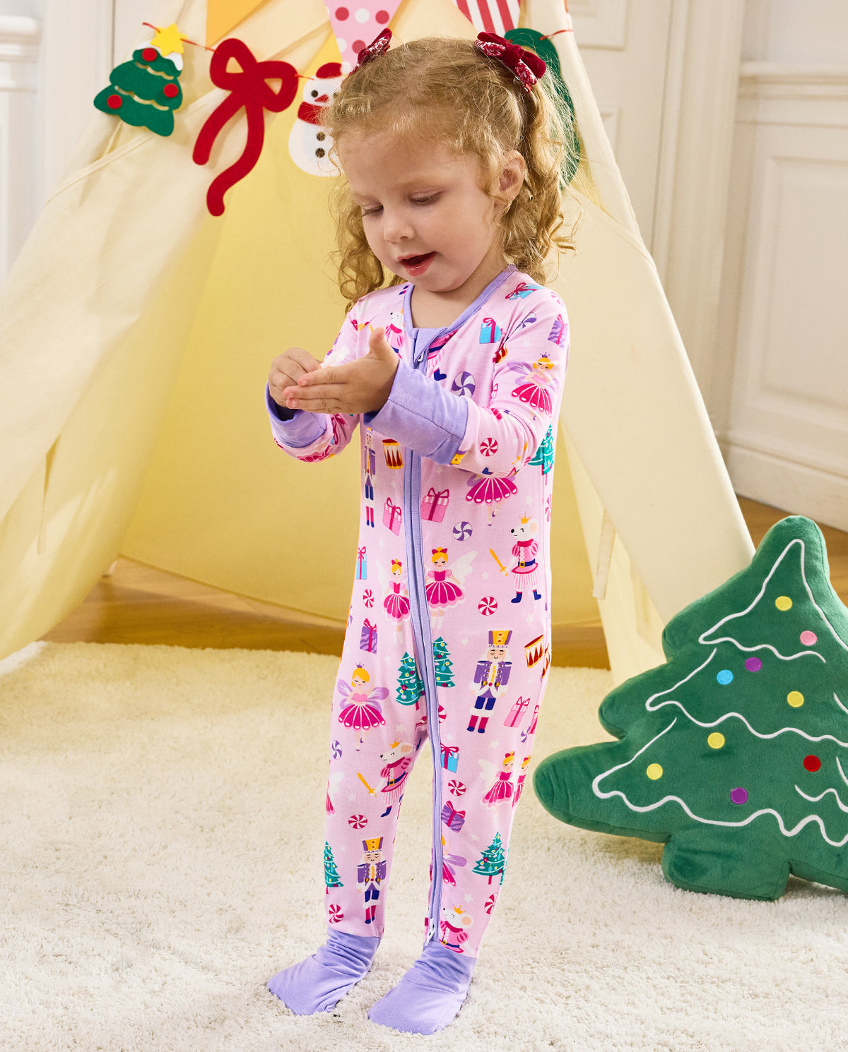 Child standing by a play tent looking at a small object in the Nutcracker Fairy romper.